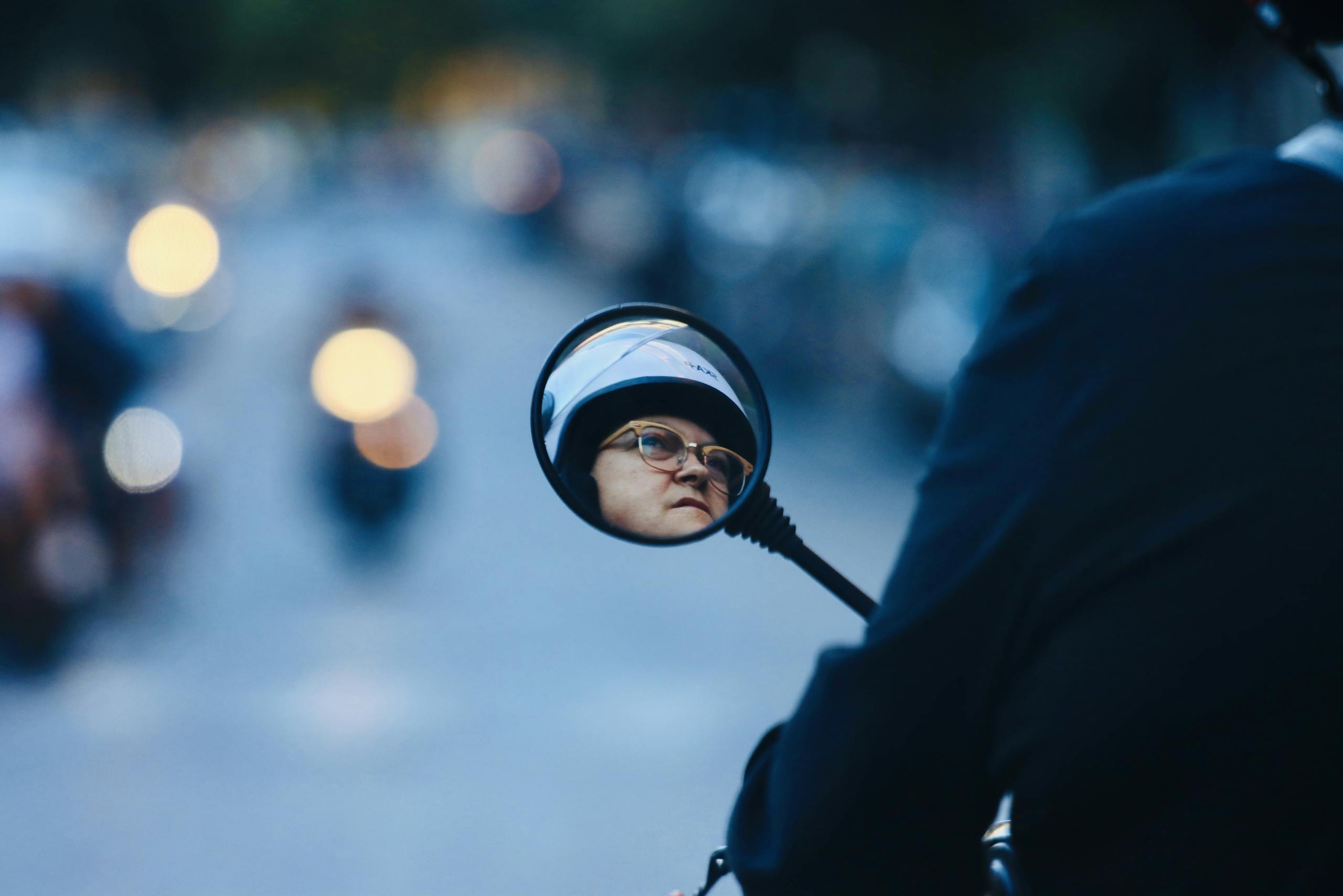 A woman wearing a helmet is reflected in a motorcycle mirror on a busy street in Naples, Italy.